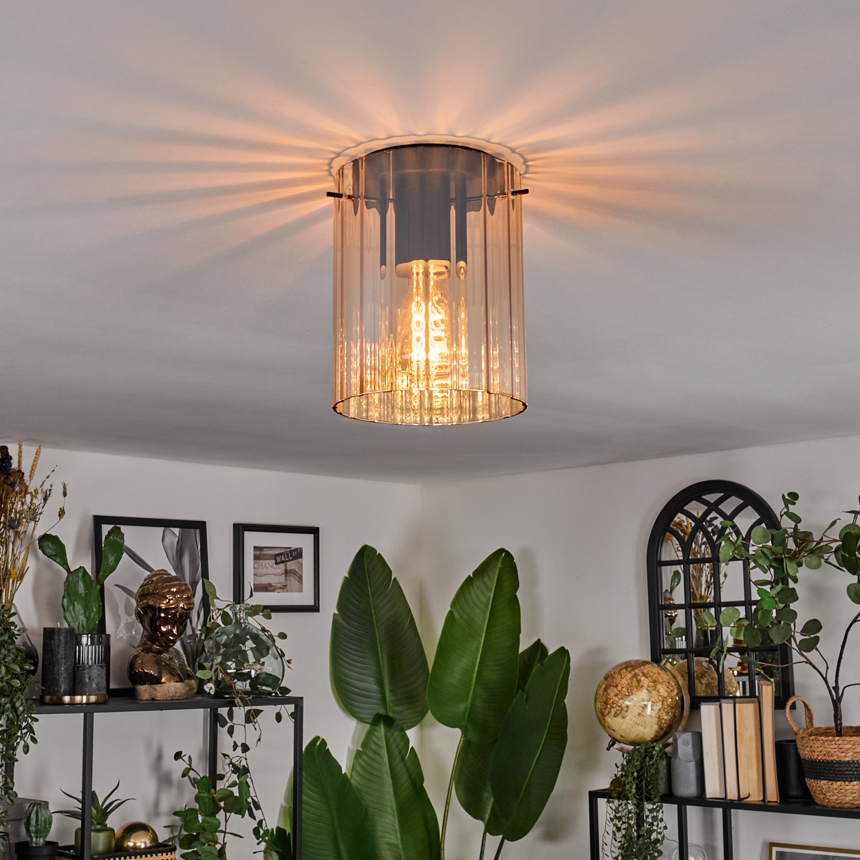 Eine Deckenlampe mit bernsteinfarbenem Glas wirft Licht. Pflanzen und Regale mit Dekoration füllen die Zimmerecken.