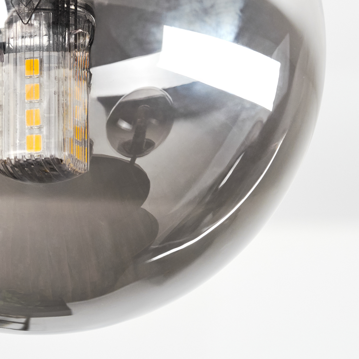 Nahaufnahme einer grauen Glaskugel, die Licht reflektiert. Links ist eine Glühbirne zu sehen, vor weißem Hintergrund.