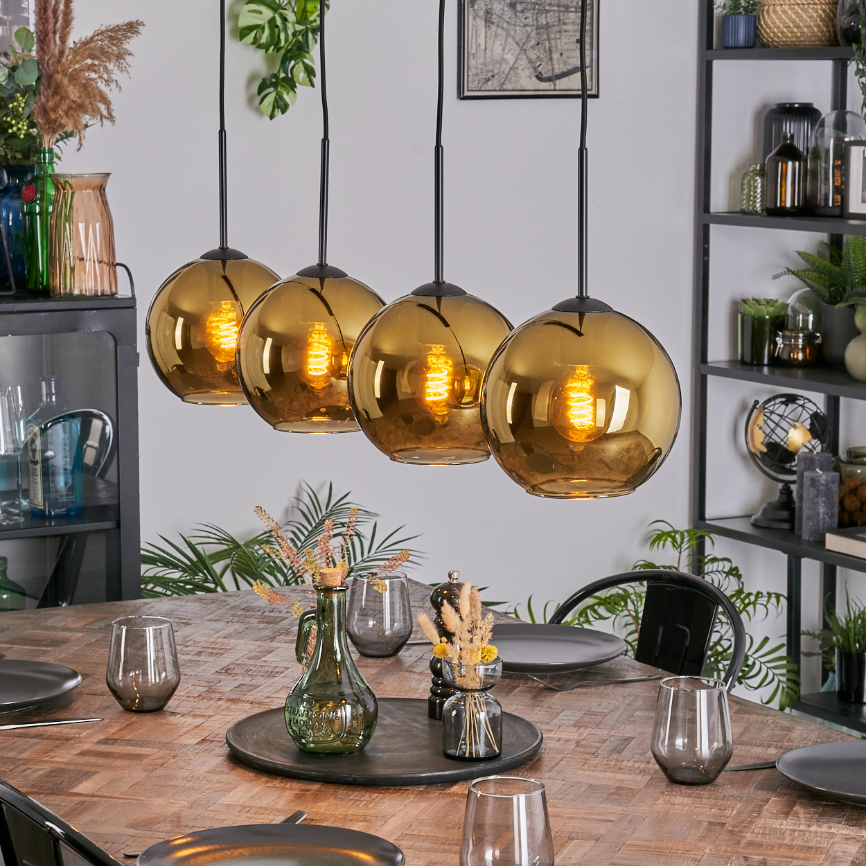Esszimmer mit Holztisch, Glaslampen und Dekorationsartikeln. Tisch mit Tellern und Gläsern. Pflanzen und Regale im Hintergrund.