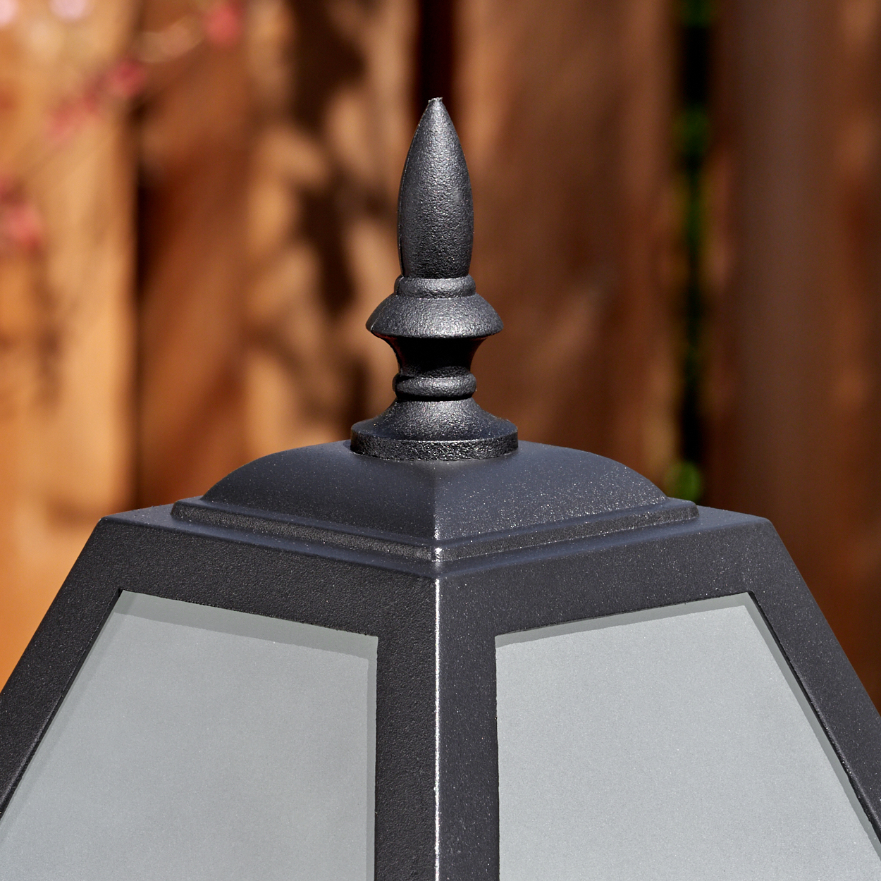 Nahaufnahme einer schwarzen Außenlampe. Die Oberseite hat eine spitze Spitze. Die Lampe hat eine geometrische Form mit Milchglasscheiben.
