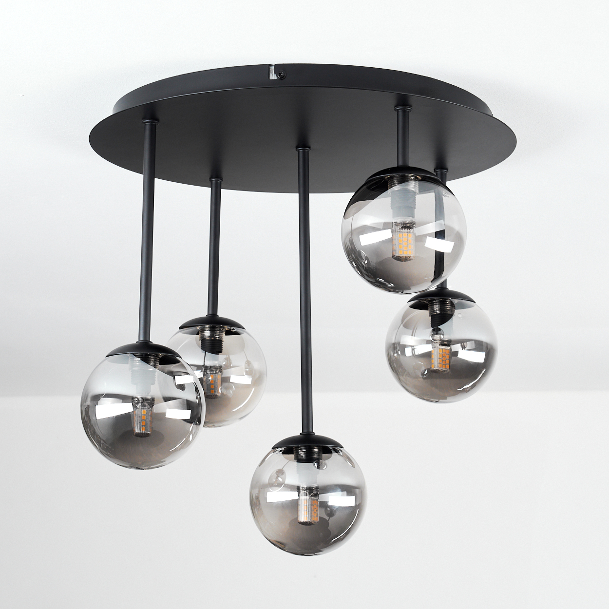 Eine moderne Deckenleuchte mit fünf kugelförmigen Glasschirmen, die von einer schwarzen runden Basis abgehängt sind.