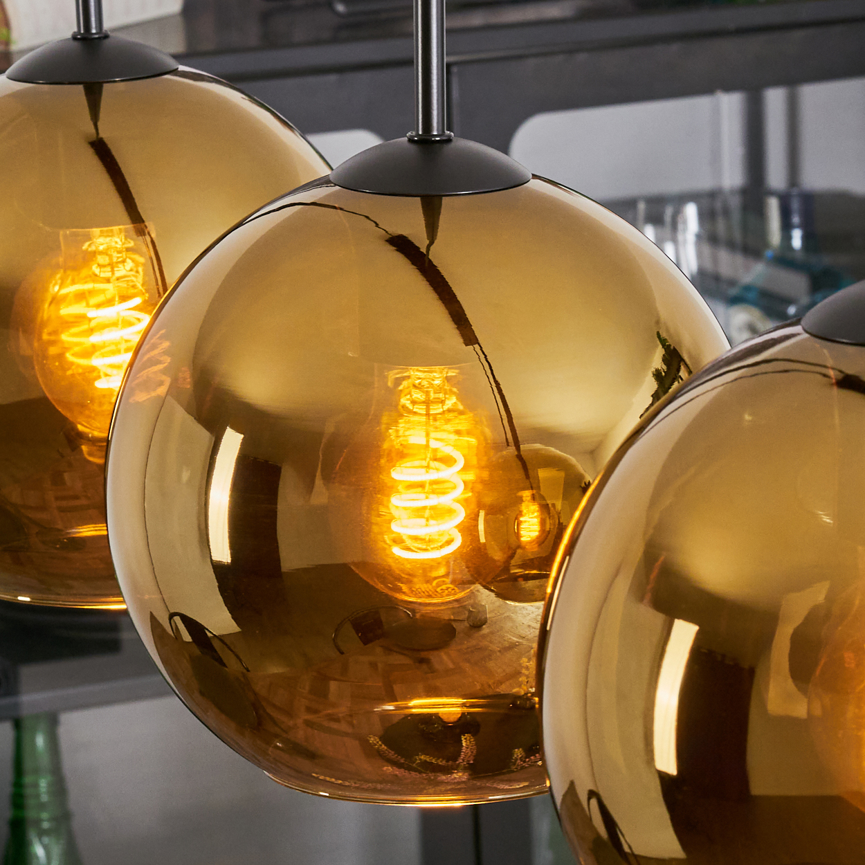 Drei goldene Pendelleuchten mit Wendelglühbirnen hängen. Der Hintergrund ist verschwommen, zeigt eine Bareinstellung.