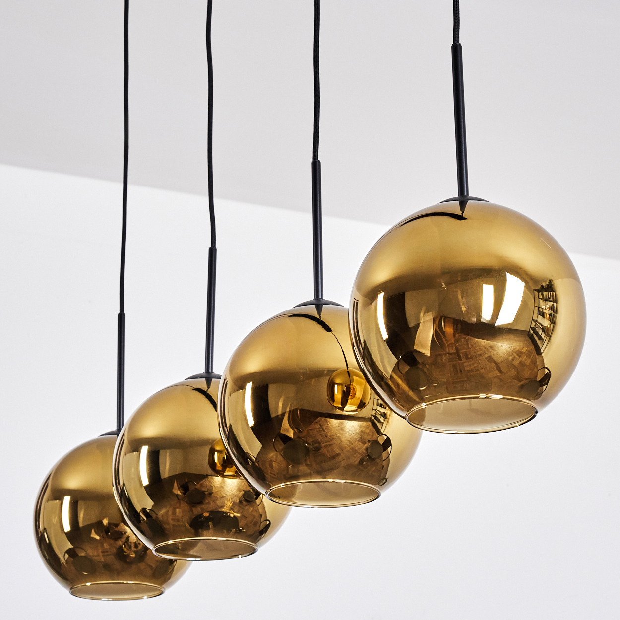 Vier goldene, kugelförmige Pendelleuchten hängen von einer weißen Decke. Jede hat ein schwarzes Kabel. Die Lichter reflektieren die Umgebung.
