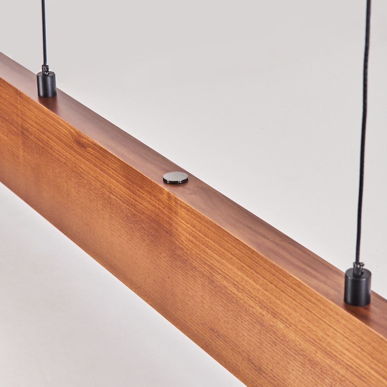 Nahaufnahme eines Holzbalkens mit zwei schwarzen Schnüren, die von oben hängen. Der Balken ist braun und hat eine Metallscheibe.