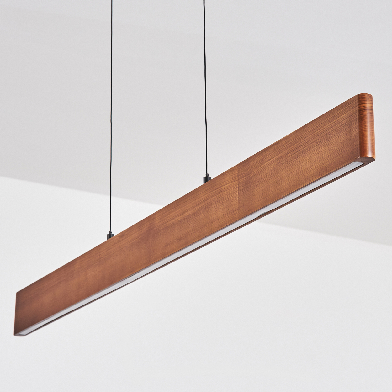 Eine rechteckige Holzleuchte hängt von der Decke. Sie hat einen Lichtstreifen an der Unterseite, der von schwarzen Drähten gehalten wird.