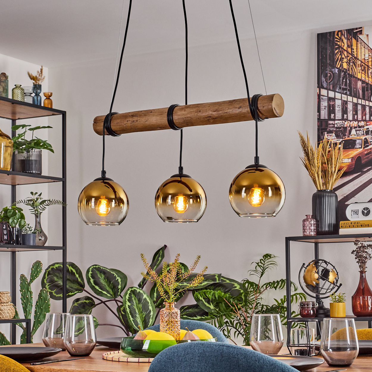 Esszimmer mit Holztisch. Drei goldene Glas-Pendelleuchten hängen darüber. Pflanzen und Dekoration befinden sich auf Regalen und dem Tisch.