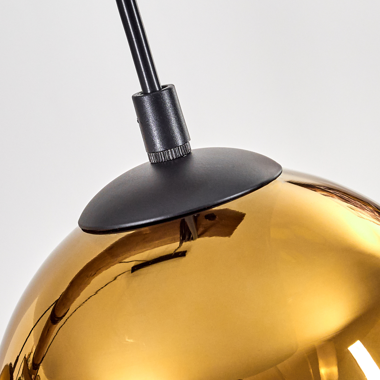 Nahaufnahme einer modernen Leuchte. Sie hat einen schwarzen Stiel und einen goldenen, reflektierenden Glasschirm. Der Hintergrund ist weiß.