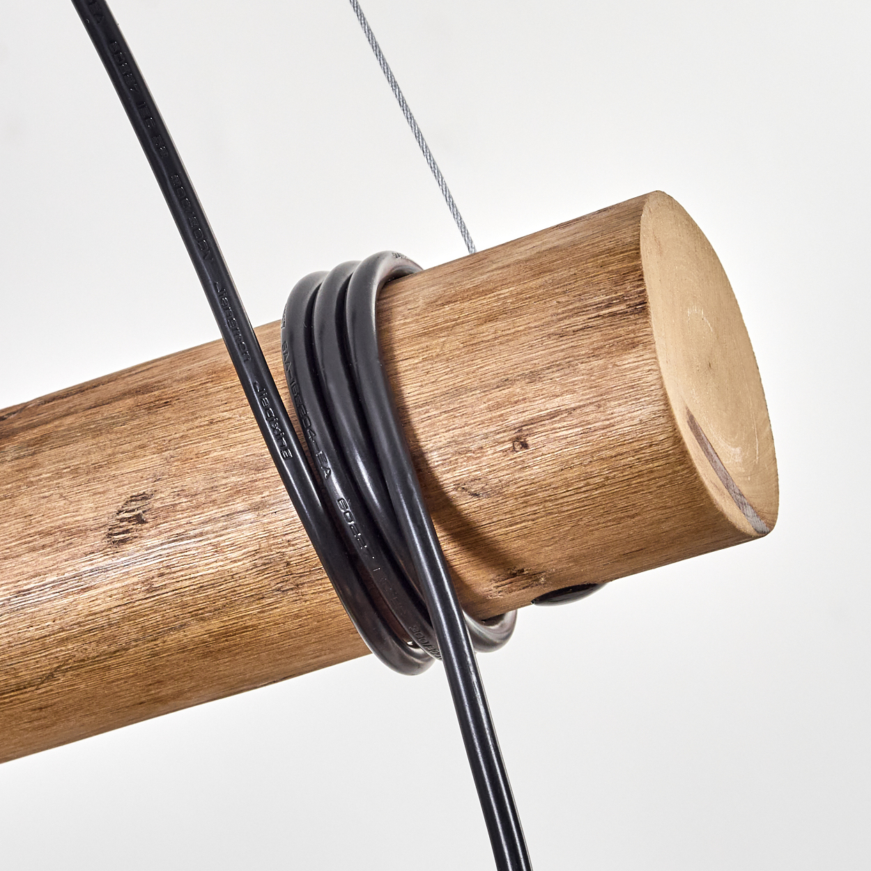 Nahaufnahme eines Holzbalkens mit schwarzen Kabeln. Ein dünner Metalldraht und mehr schwarzes Kabel sind sichtbar.