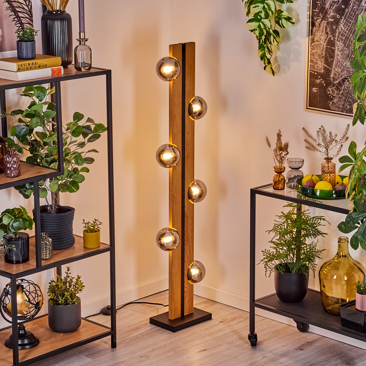 Ein modernes Wohnzimmer mit Stehlampe, Regalen mit Pflanzen und Dekor sowie einem Wagen. Die Lampe hat Glaskugel-Lichter.