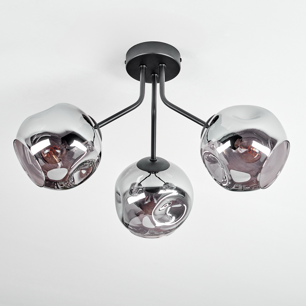 Eine moderne Deckenleuchte mit drei unregelmäßig geformten, rauchigen Glaskugeln. Sie hat schwarze Metallarme und eine Deckenhalterung auf weißem Hintergrund.