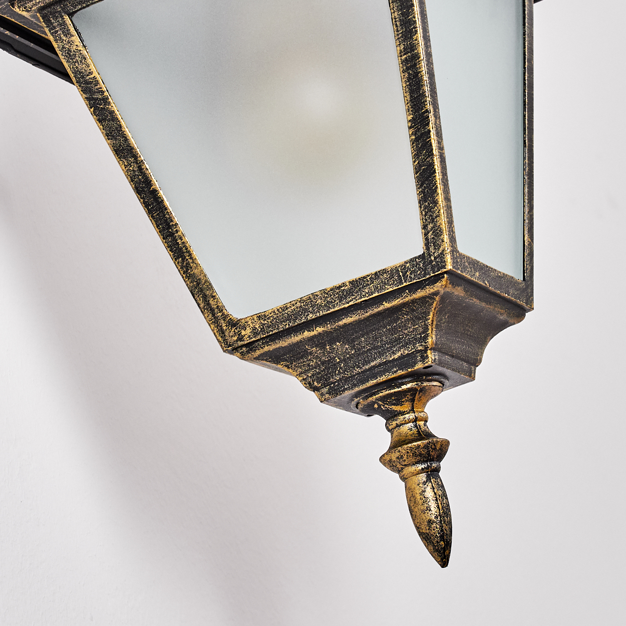 Nahaufnahme einer goldenen Vintage-Laterne an einer weißen Wand. Die Laterne hat Milchglasscheiben und komplizierte Details.