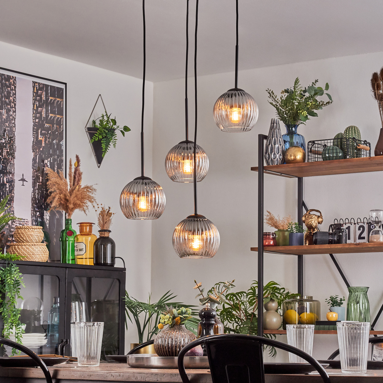 Esszimmer mit Hängelampen, Regalen mit Dekor und einem Tisch zum Essen. Pflanzen und verschiedene Vasen sind vorhanden.