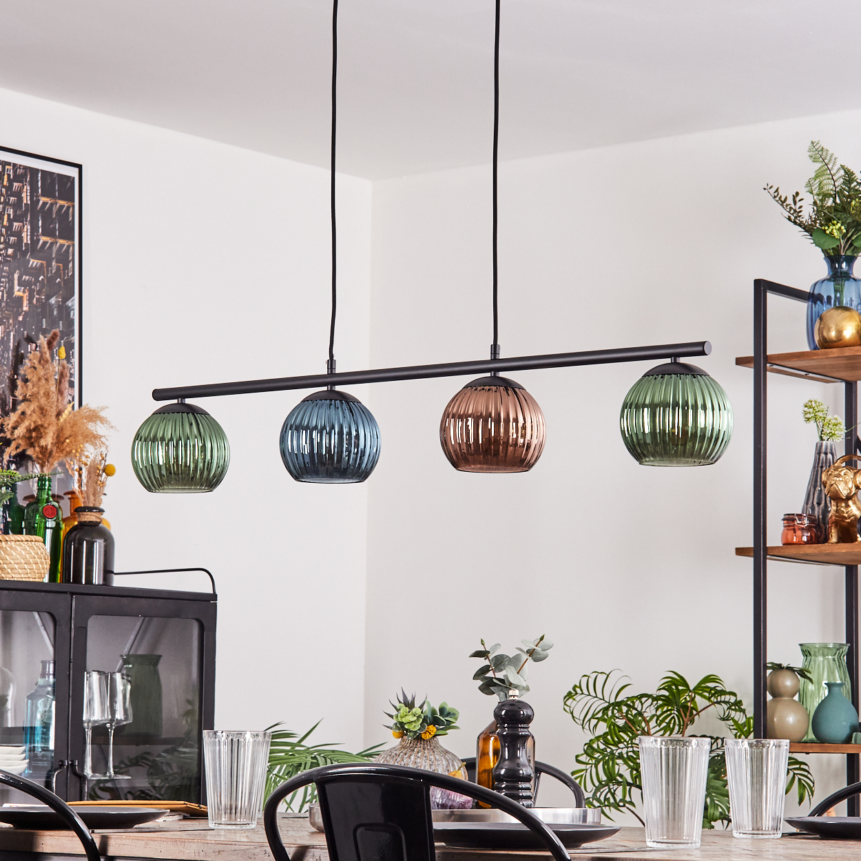 Ein Esszimmer mit einem gedeckten Tisch. Über dem Tisch hängt eine schwarze Leuchte mit vier farbigen Glaskugeln.