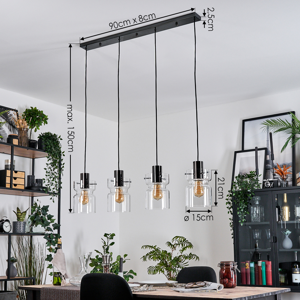 Ein modernes Esszimmer-Setup. Eine schwarze rechteckige Leuchte mit vier Hängelampen. Pflanzen und Möbel sind ebenfalls im Hintergrund zu sehen.