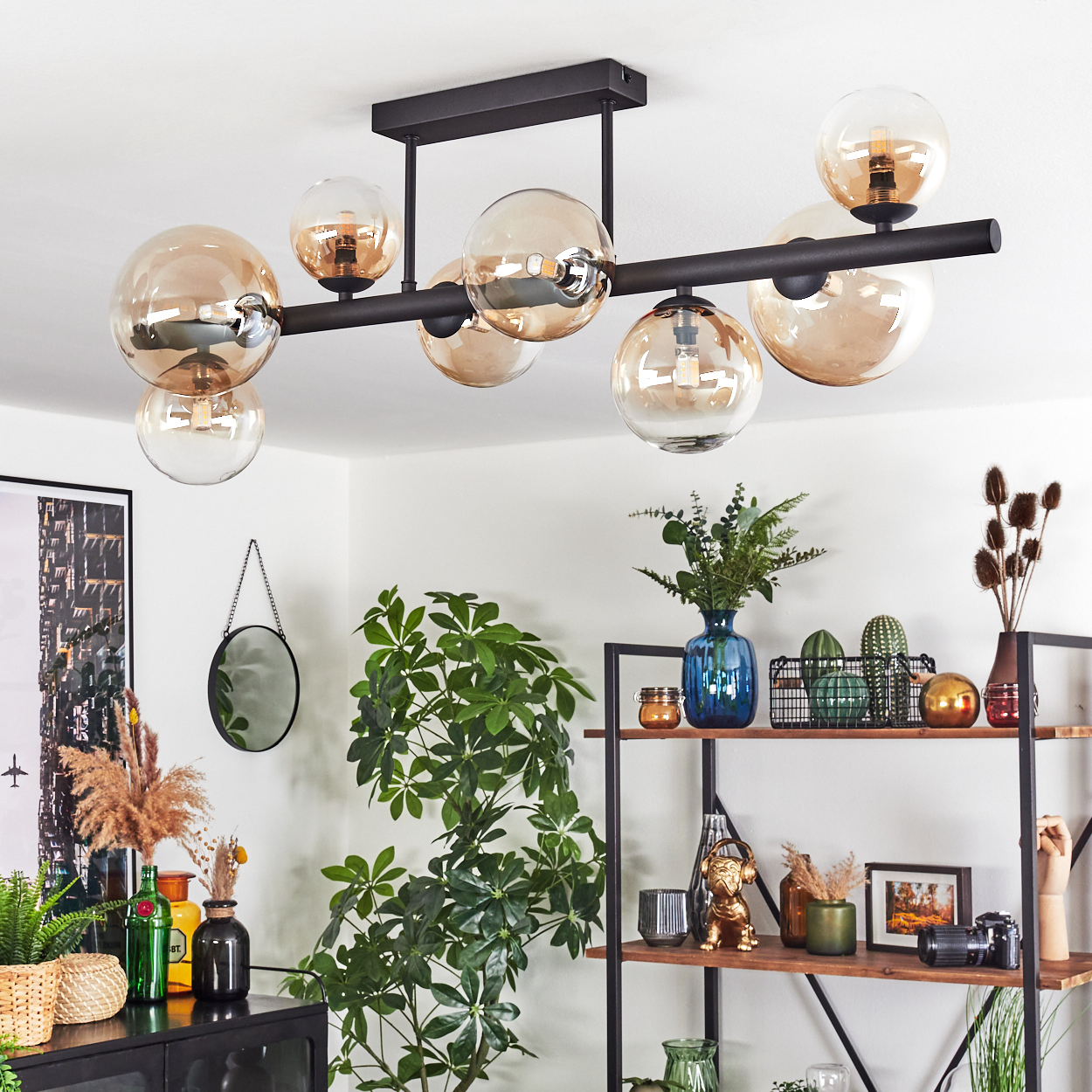 Ein modernes Wohnzimmer mit schwarzem Kronleuchter, Pflanzen, Spiegel und Regalen mit Dekorationen.