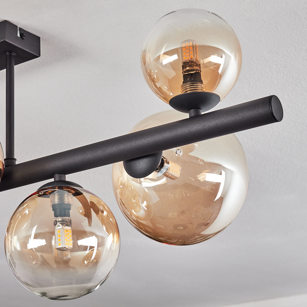 Moderne schwarze Deckenleuchte mit drei bernsteinfarbenen Glaskugeln, jede mit einer sichtbaren LED-Glühbirne. Die Decke ist weiß.