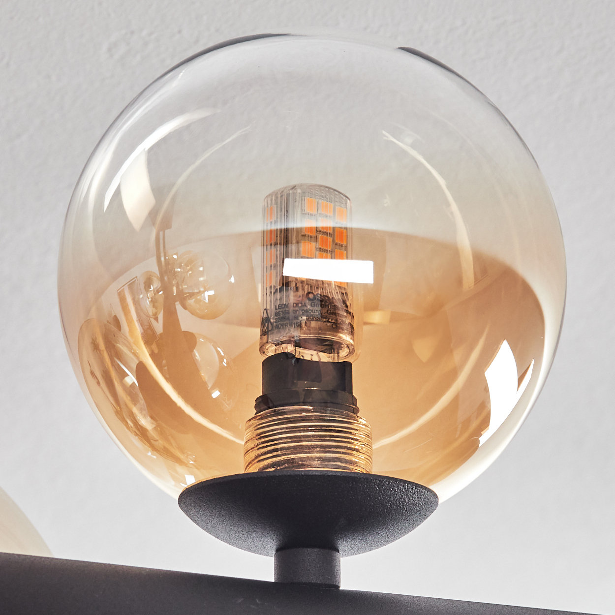 Nahaufnahme einer Leuchte mit einer transparenten Glaskugel und einer warmtonigen Glühbirne, vor weißem Hintergrund.