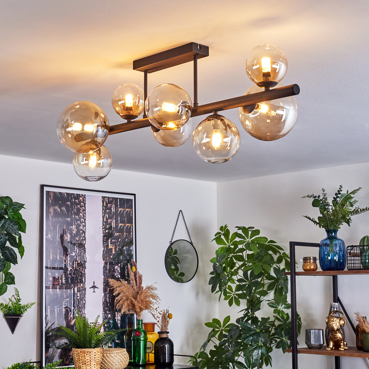 Eine moderne Deckenlampe mit Glaskugeln hängt im Raum. Darunter sind Pflanzen, ein Spiegel und ein Bild zu sehen.