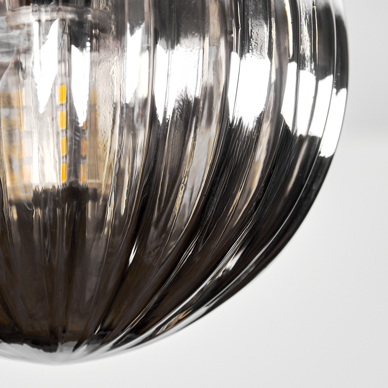 Nahaufnahme einer Glasleuchte mit vertikalen Rillen. Das Glas ist klar und reflektiert Licht. Der Hintergrund ist weiß.