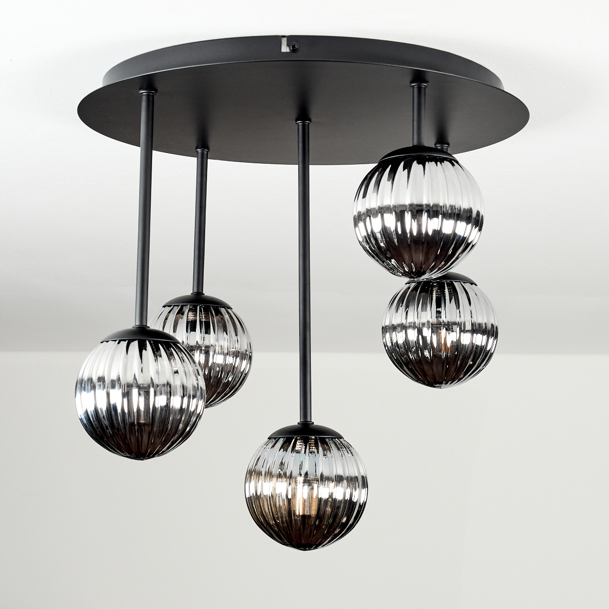 Eine moderne Deckenleuchte mit fünf Glaskugelleuchten hängt von einer schwarzen kreisförmigen Basis. Die Kugeln haben ein geripptes Design.