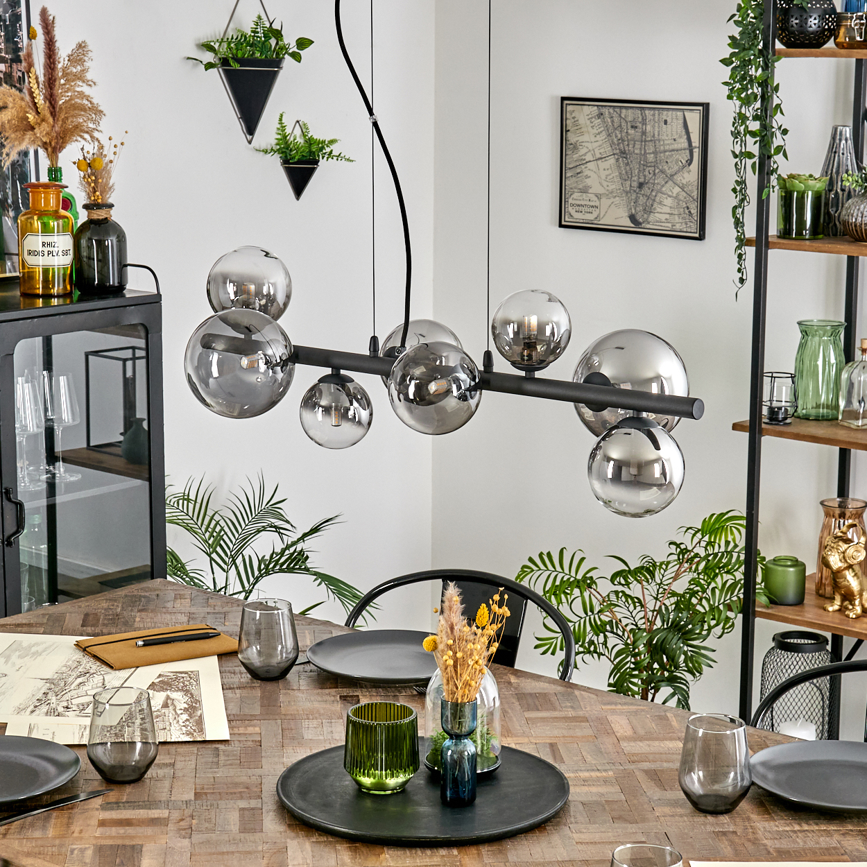 Esszimmer mit Holztisch, Glaskugelleuchten und verschiedenen Dekorationsartikeln, darunter Pflanzen und Vasen.