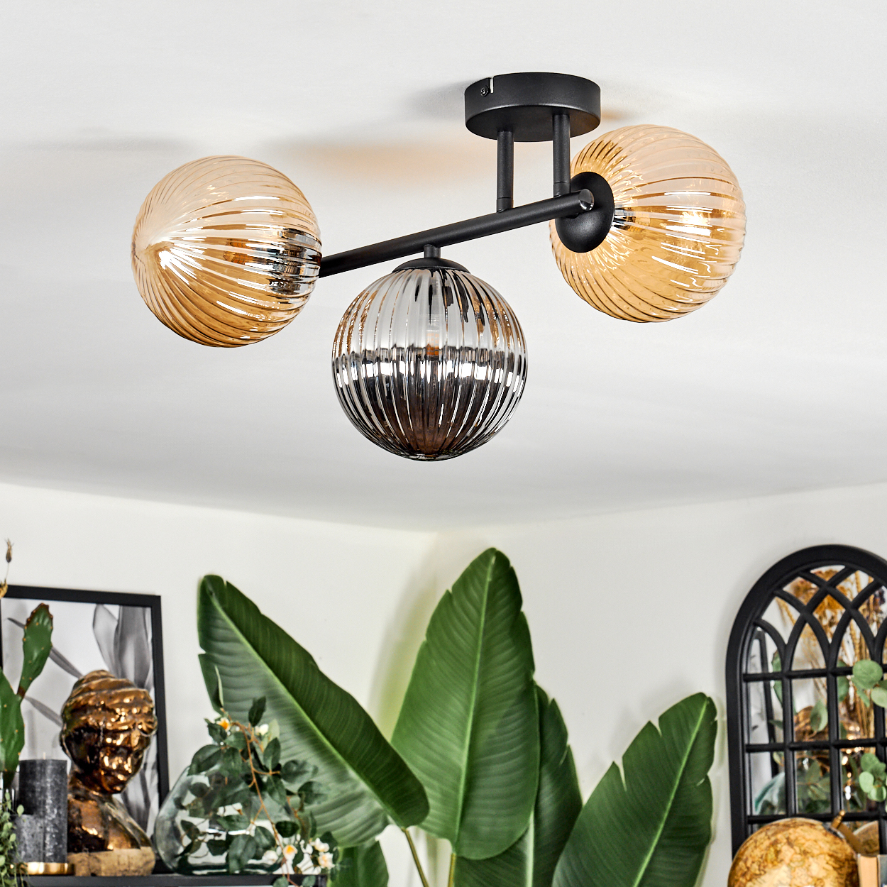 Eine moderne Deckenleuchte mit drei kugelförmigen Lampen. Die Lampen haben ein geripptes Design, zwei sind bernsteinfarben und eine ist silber.