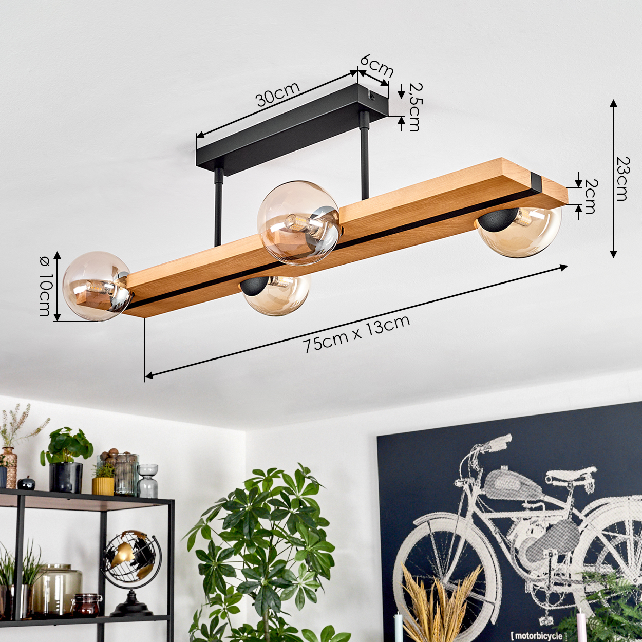 Eine moderne Deckenlampe mit vier Glaskugeln und einem Holzbalken. Der Hintergrund zeigt ein schwarzes Regal und ein Motorradgemälde.