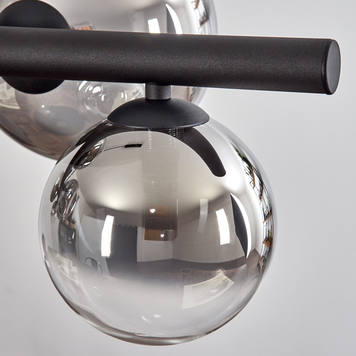 Eine moderne Lampe mit zwei silbernen Kugeln und einem schwarzen Balken. Die Kugeln reflektieren die Umgebung. Die Lampe steht vor einer weißen Wand.