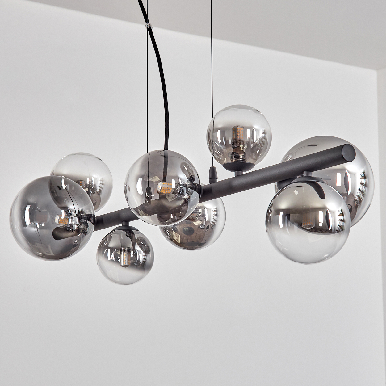 Eine moderne Deckenleuchte mit mehreren kugelförmigen Glasschirmen in verschiedenen Größen. Das Gestell ist schwarz, mit weißem Hintergrund.