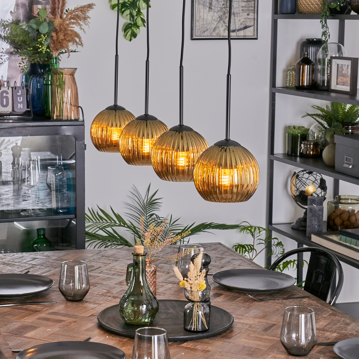 Esszimmer mit Holztisch. Vier Hängelampen. Teller, Gläser und Dekorationsartikel auf dem Tisch. Regale mit Deko im Hintergrund.