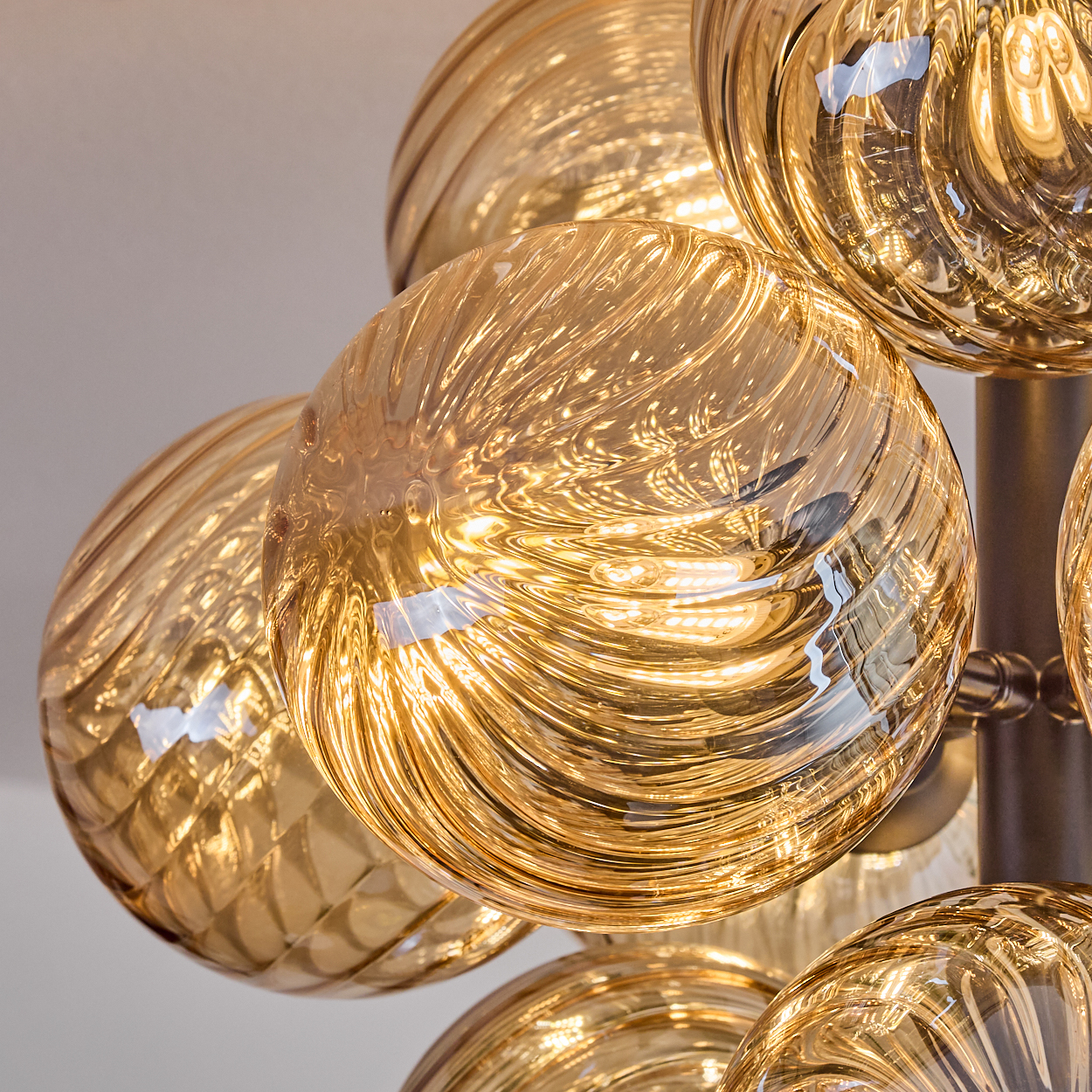 Nahaufnahme eines Kronleuchters mit mehreren goldenen, strukturierten Glaskugeln. Das Licht reflektiert sich in den Wirbelmustern.