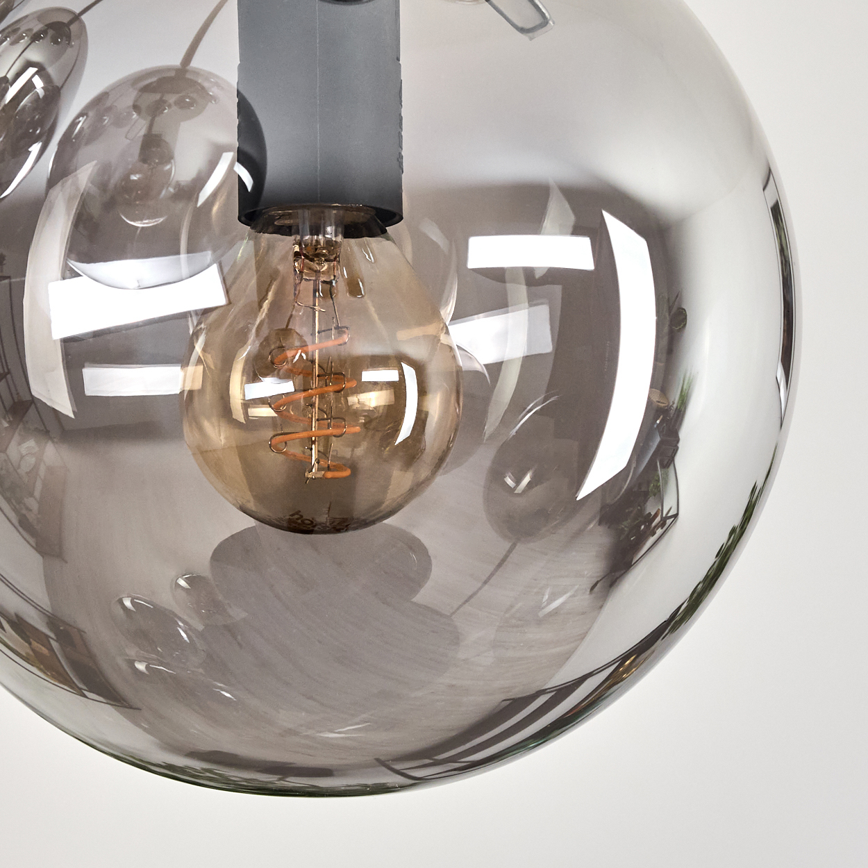 Nahaufnahme einer transparenten, kugelförmigen Leuchte mit einer sichtbaren Glühbirne. Das Licht spiegelt die Umgebung wider.