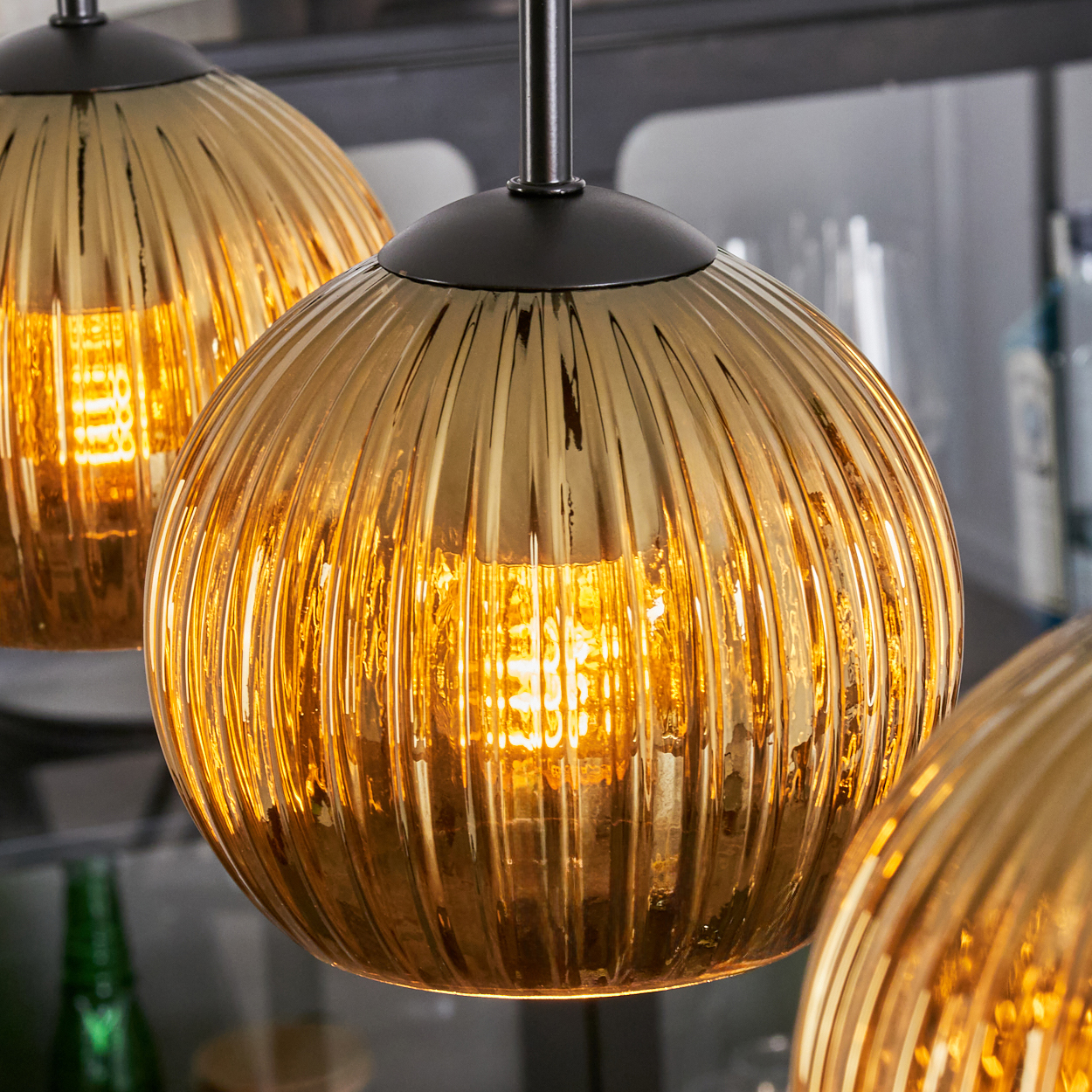 Nahaufnahme von drei goldenen, gerippten Glas-Hängelampen. Jede Glühbirne leuchtet hell.