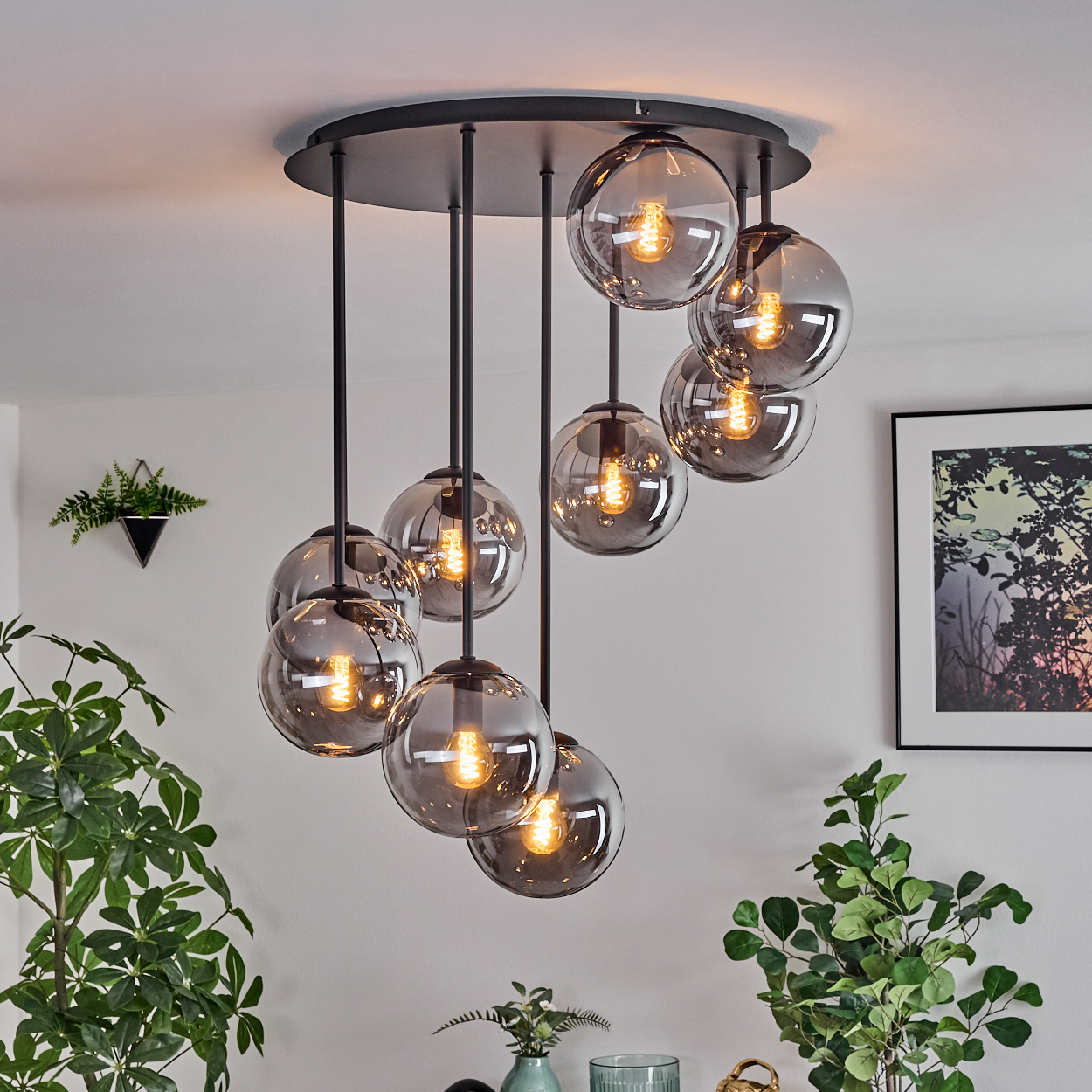 Eine moderne Deckenleuchte mit neun rauchfarbenen Glaskugelleuchten hängt von der Decke. Pflanzen und gerahmte Kunst schmücken den Raum.