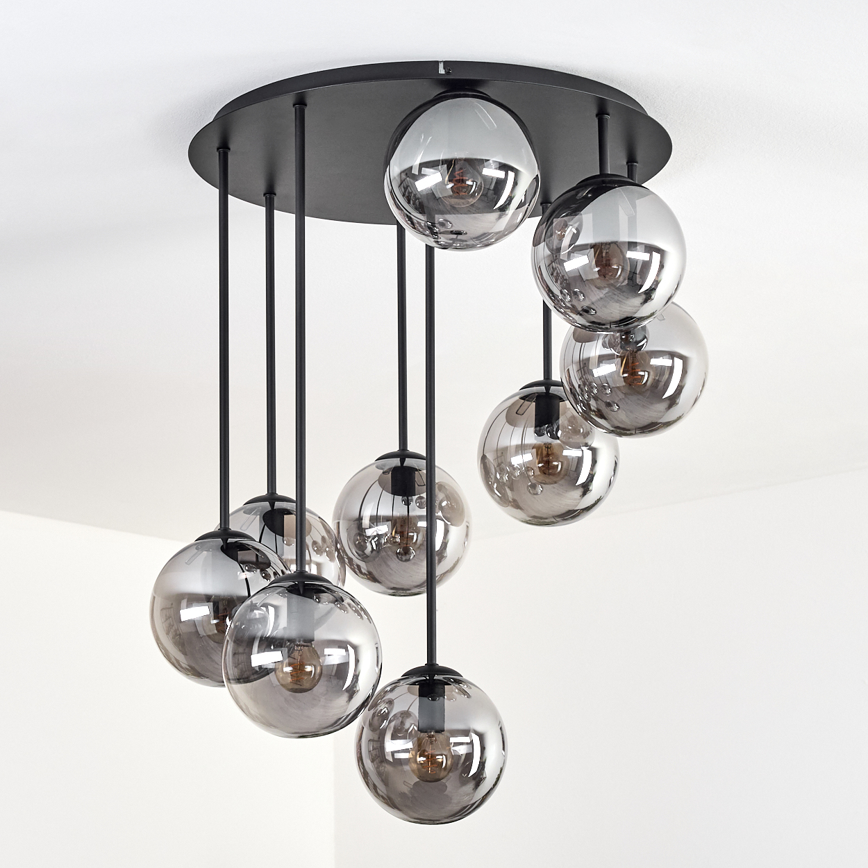 Eine moderne Deckenleuchte mit mehreren kugelförmigen, grauen Glasschirmen hängt an einer schwarzen Deckenhalterung. Der Hintergrund ist weiß.