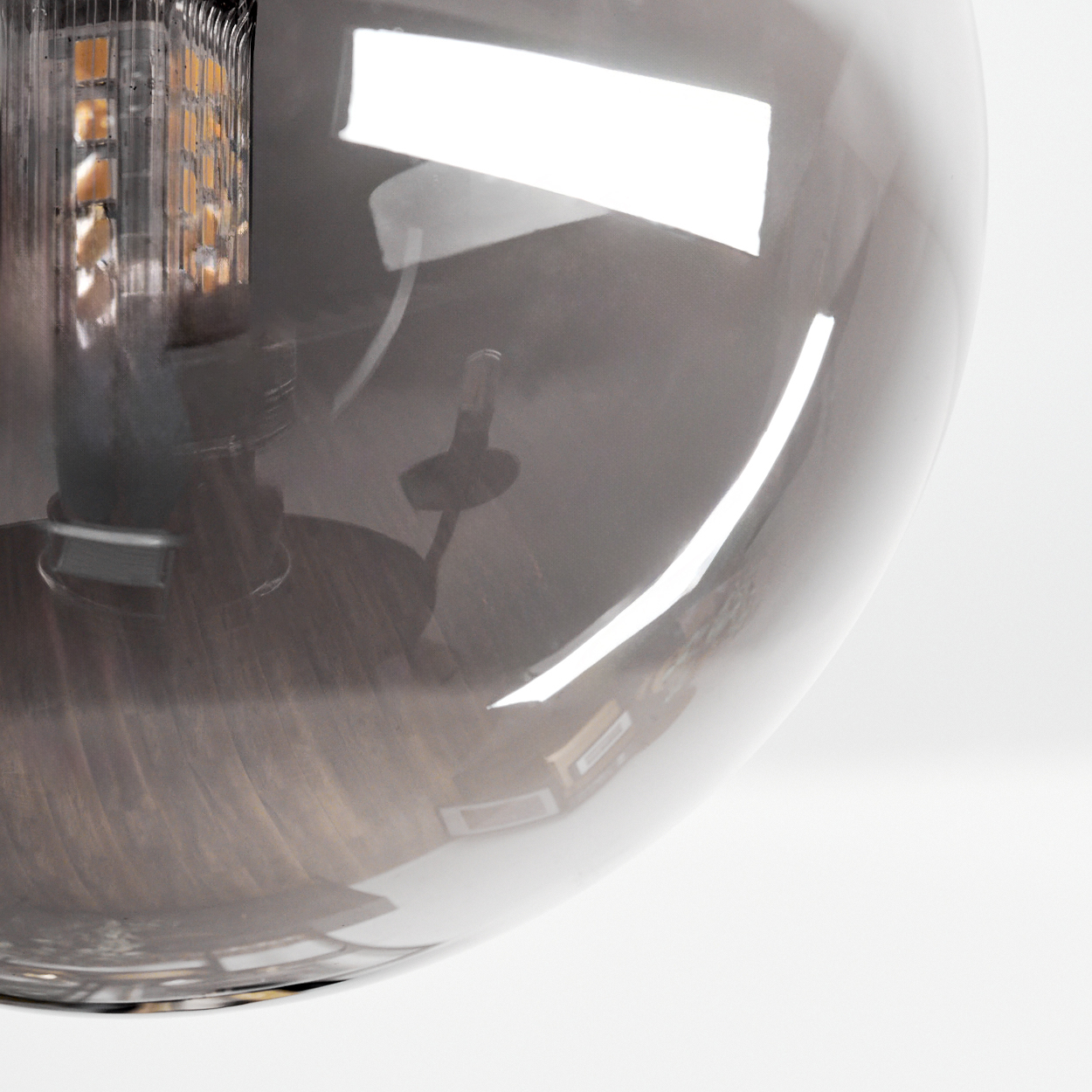Nahaufnahme einer grauen Glasbirne mit sichtbarer interner Leuchte. Die Birne reflektiert Licht und hat einen weißen Hintergrund.