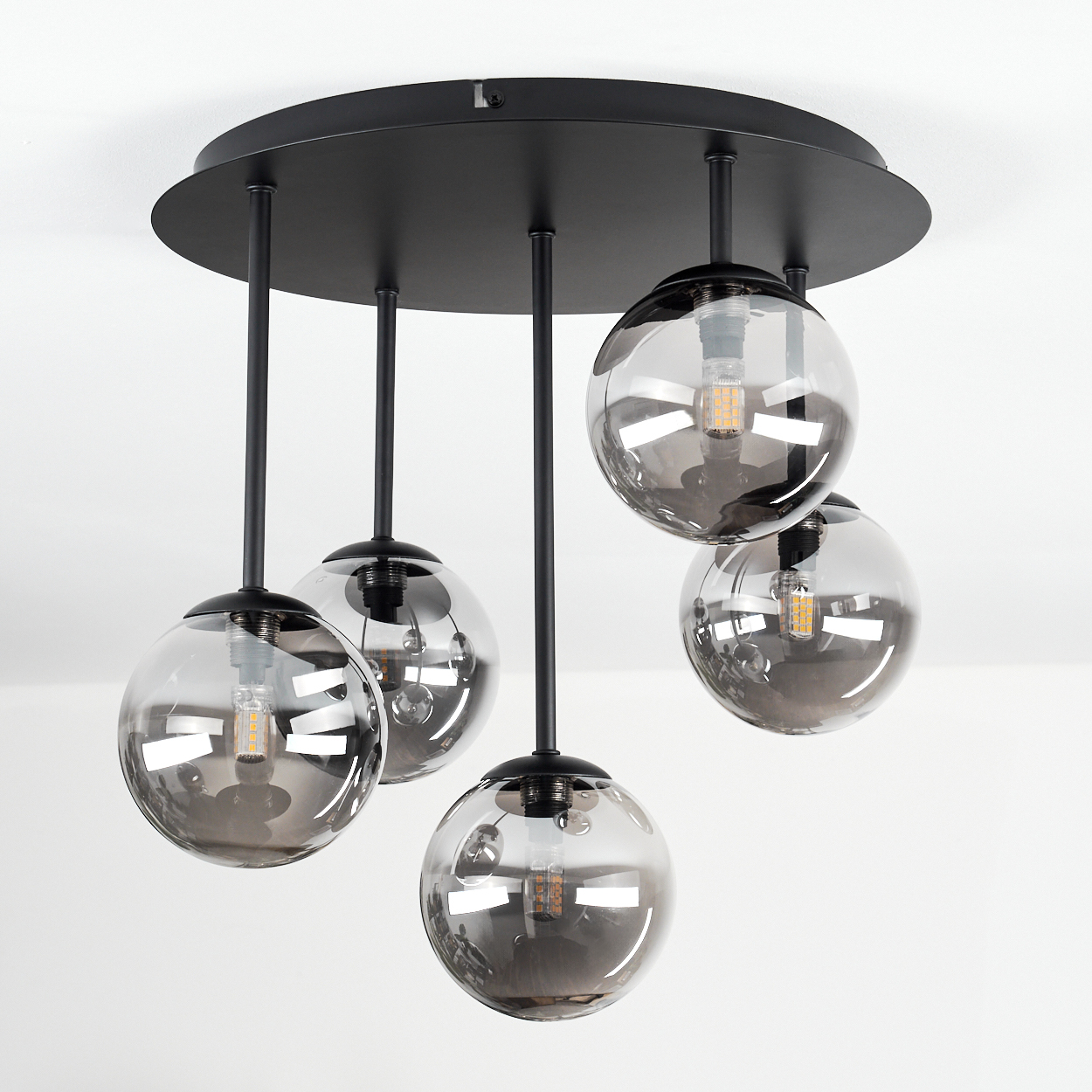 Eine moderne schwarze Pendelleuchte mit fünf rauchigen Glaskugeln, jede mit einer sichtbaren Glühbirne, hängt an einer weißen Decke.