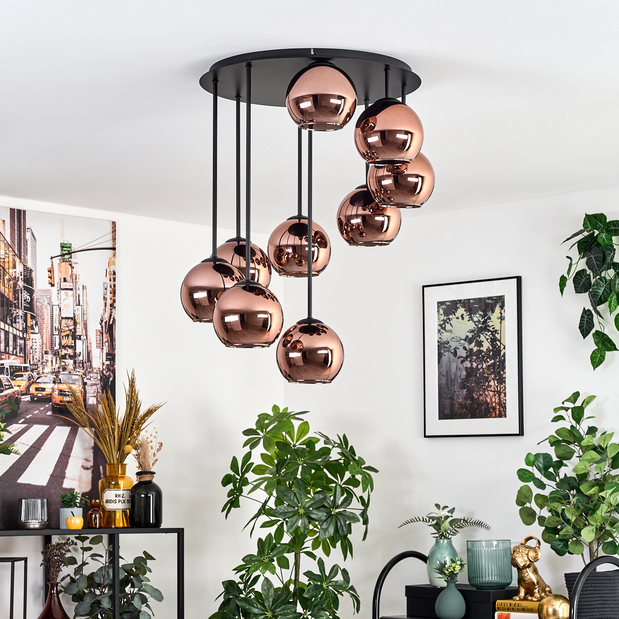 Eine moderne Deckenlampe mit kupferfarbenen Kugeln hängt von der Decke. Pflanzen und gerahmte Kunst schmücken den Raum. Ein Stadtbildgemälde ist sichtbar.