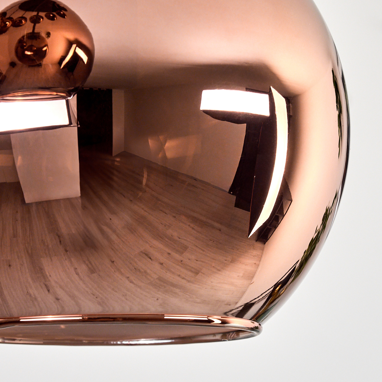 Eine kupferfarbene Pendelleuchte spiegelt einen Raum mit Holzböden und weißen Wänden wider. Lichter spiegeln sich in der Oberfläche der Lampe.