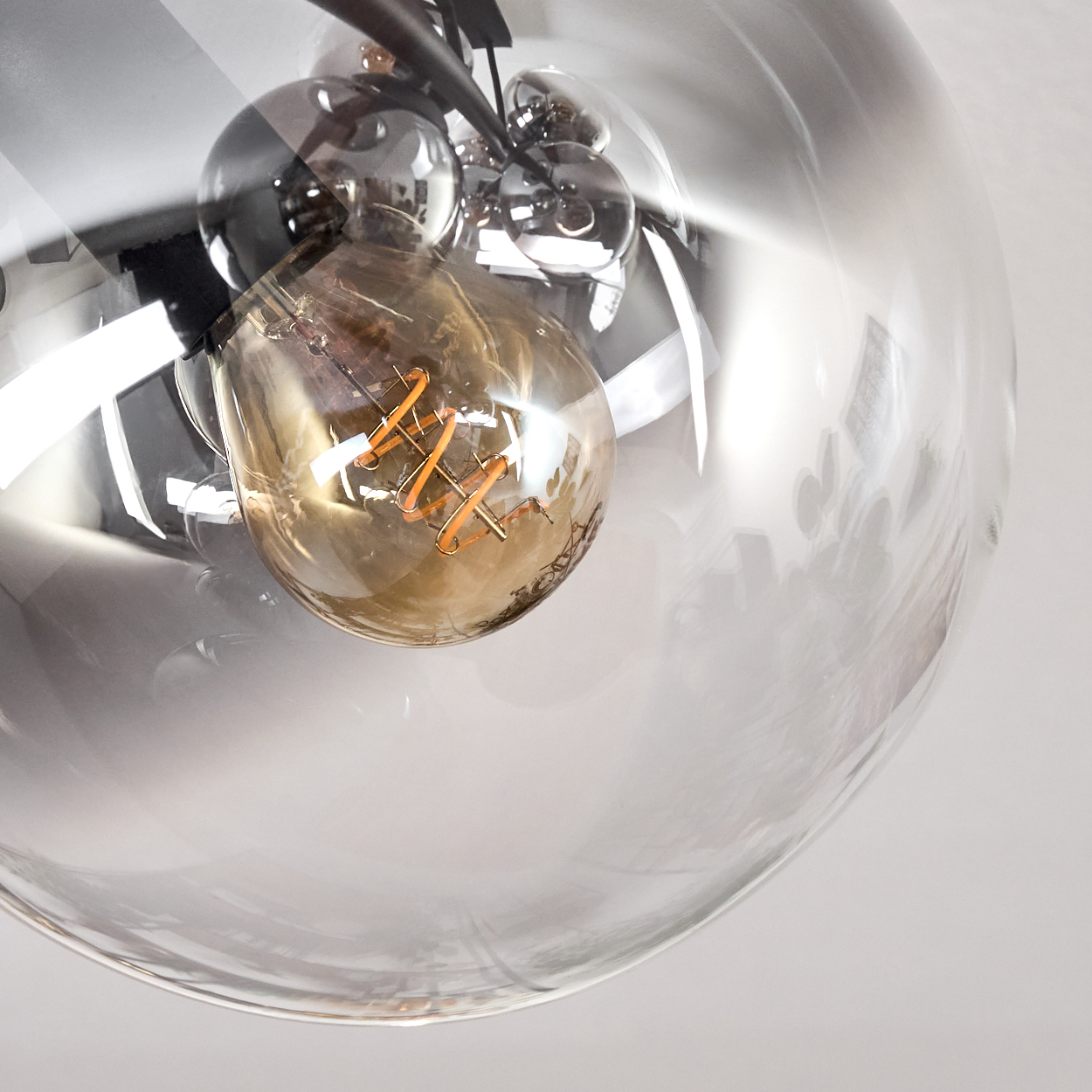 Nahaufnahme einer Leuchte mit einer großen Glaskugel, die eine Glühbirne mit glühendem Glühfaden umschließt. Andere, kleinere Glaskugeln sind sichtbar.