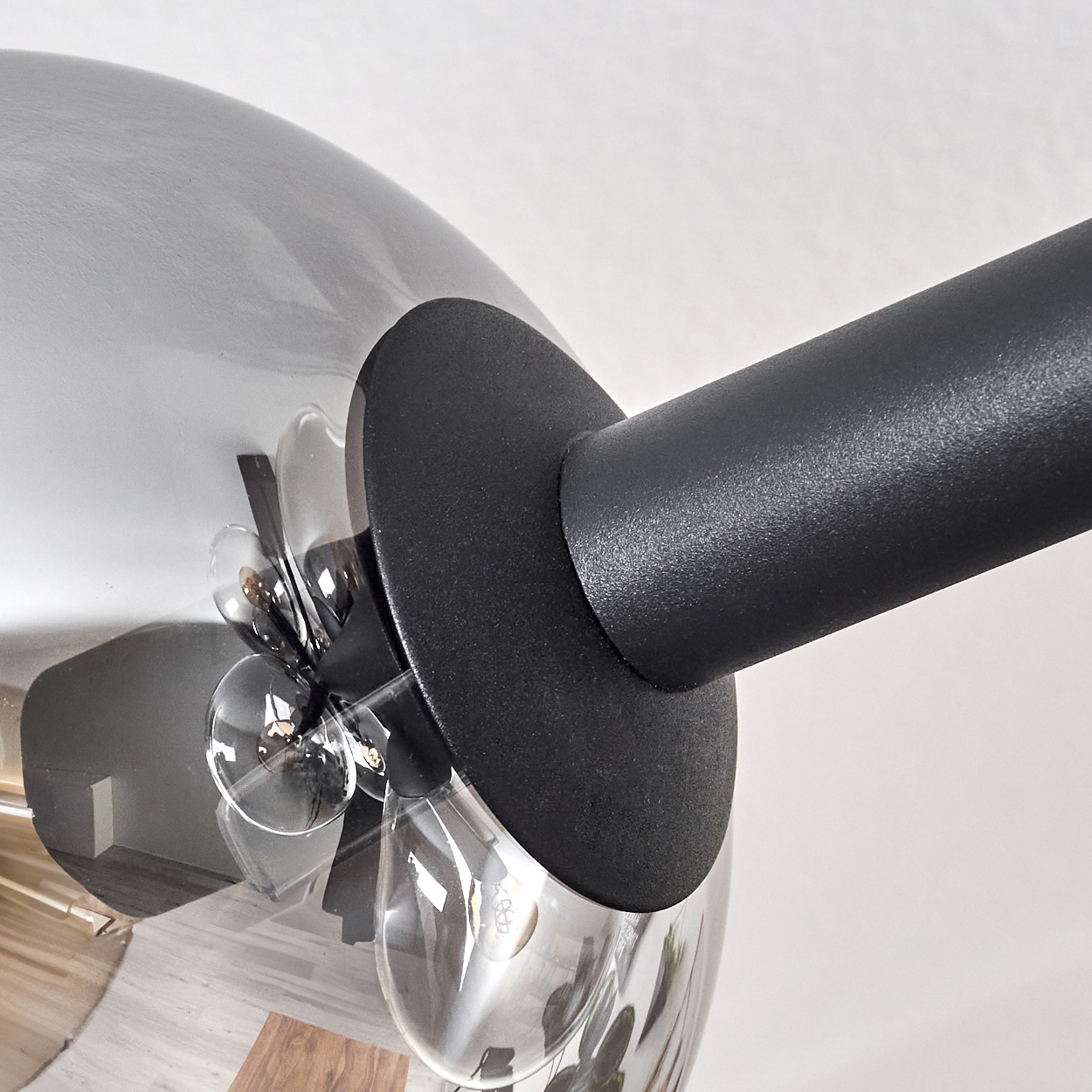 Nahaufnahme einer modernen Lampe. Sie hat einen runden Glasschirm, eine schwarze Halterung und einen schwarzen Arm. Der Hintergrund ist weiß.