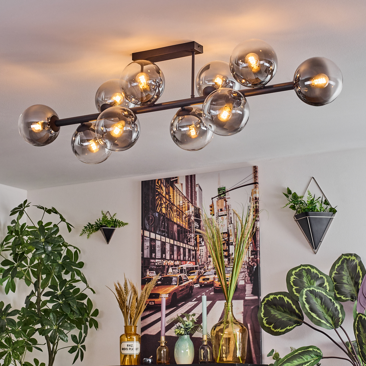 Ein modernes Wohnzimmer mit einzigartigem Kronleuchter, Kunstwerk einer Stadtszene und Topfpflanzen.