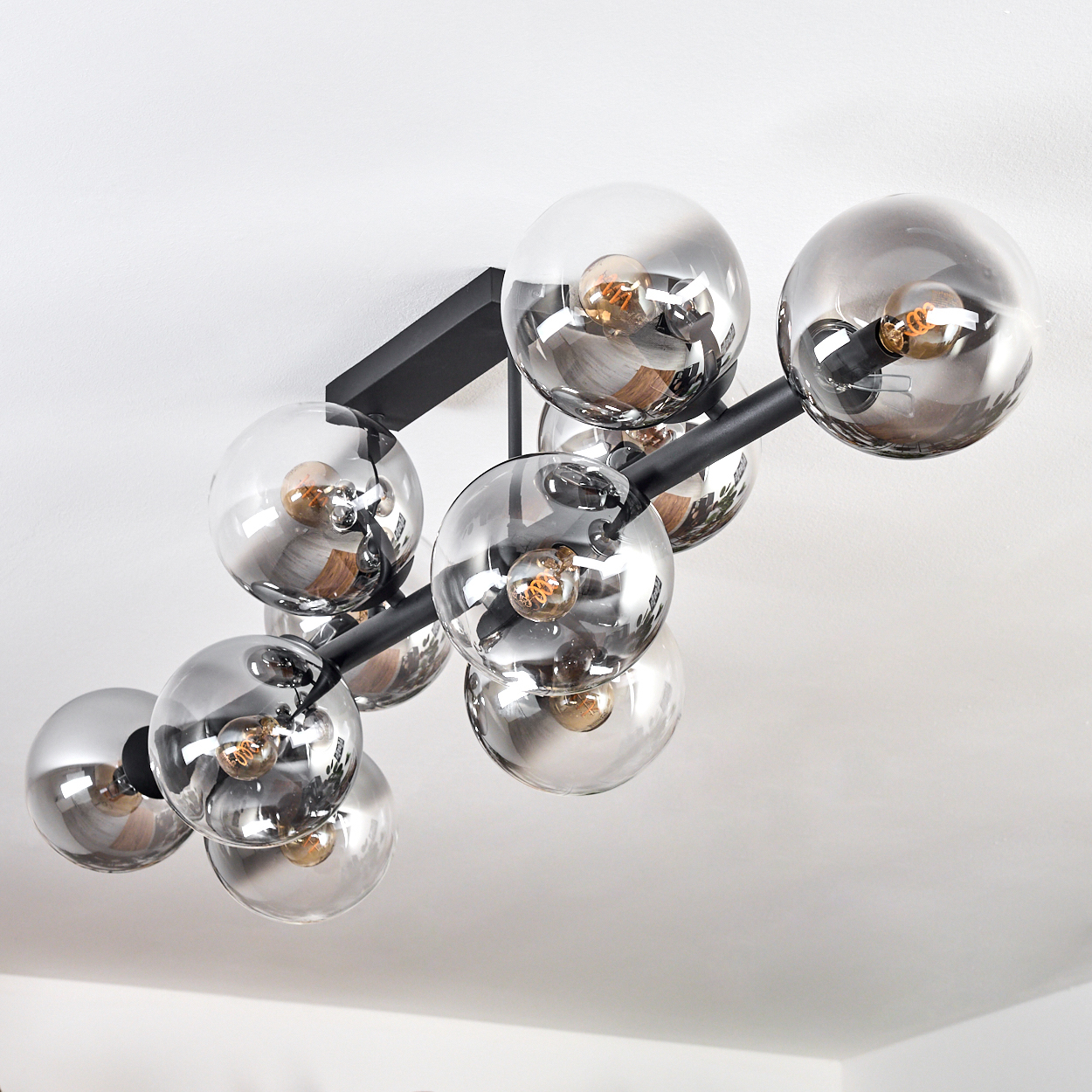 Eine moderne Deckenleuchte mit mehreren transparenten, kugelförmigen Glühbirnen an schwarzen Metallarmen an einer weißen Decke.