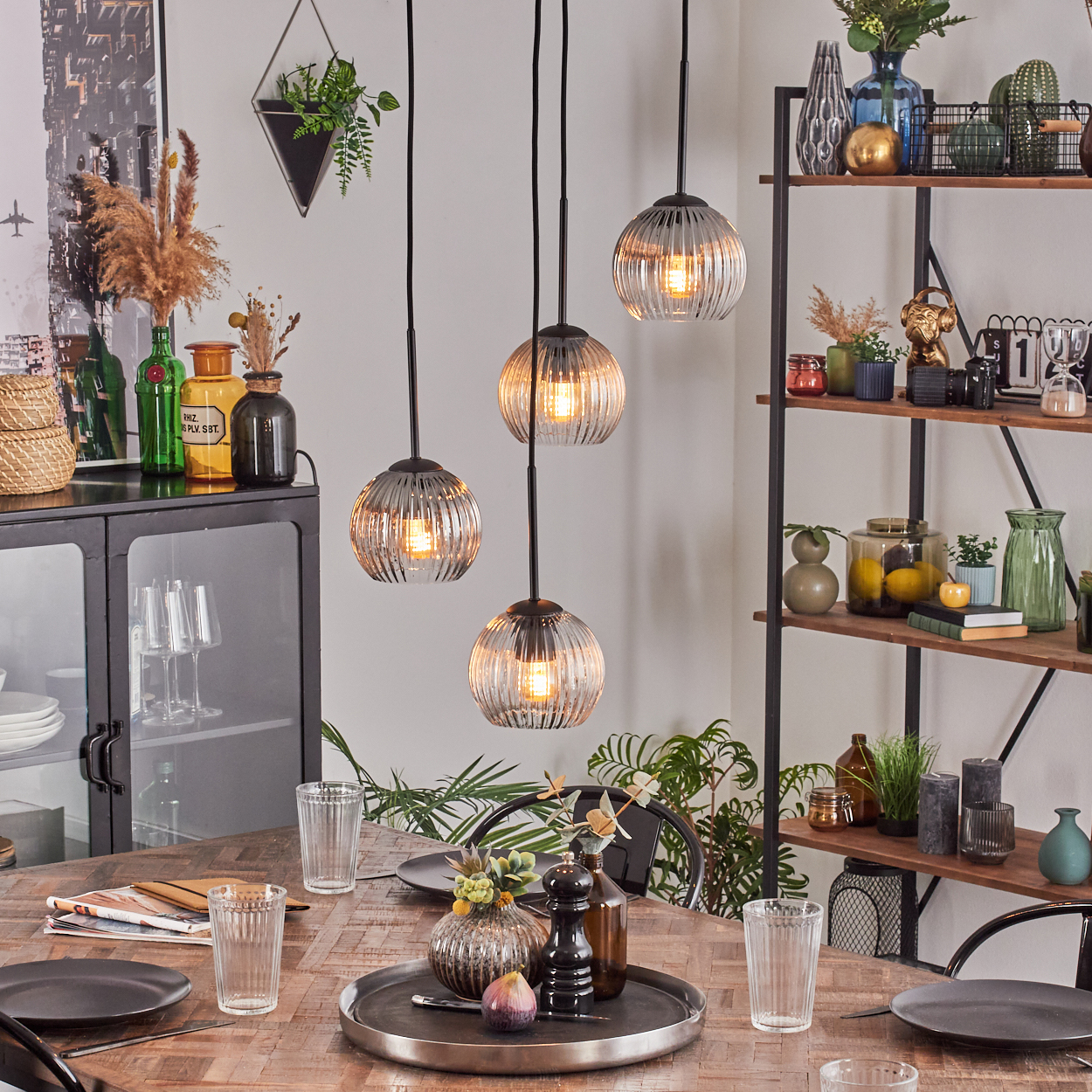 Esszimmer mit Hängelampen, gedecktem Tisch und Regalen mit Dekoration. Enthält Gläser, Teller und Pflanzen.