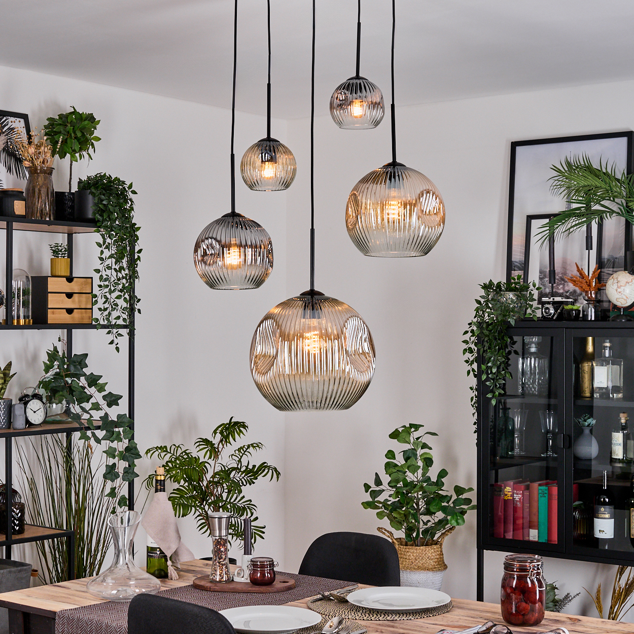 Esszimmer mit hängenden Kugelleuchten. Tisch mit Tellern, Pflanzen und einem schwarzen Schrank mit Dekor im Hintergrund.