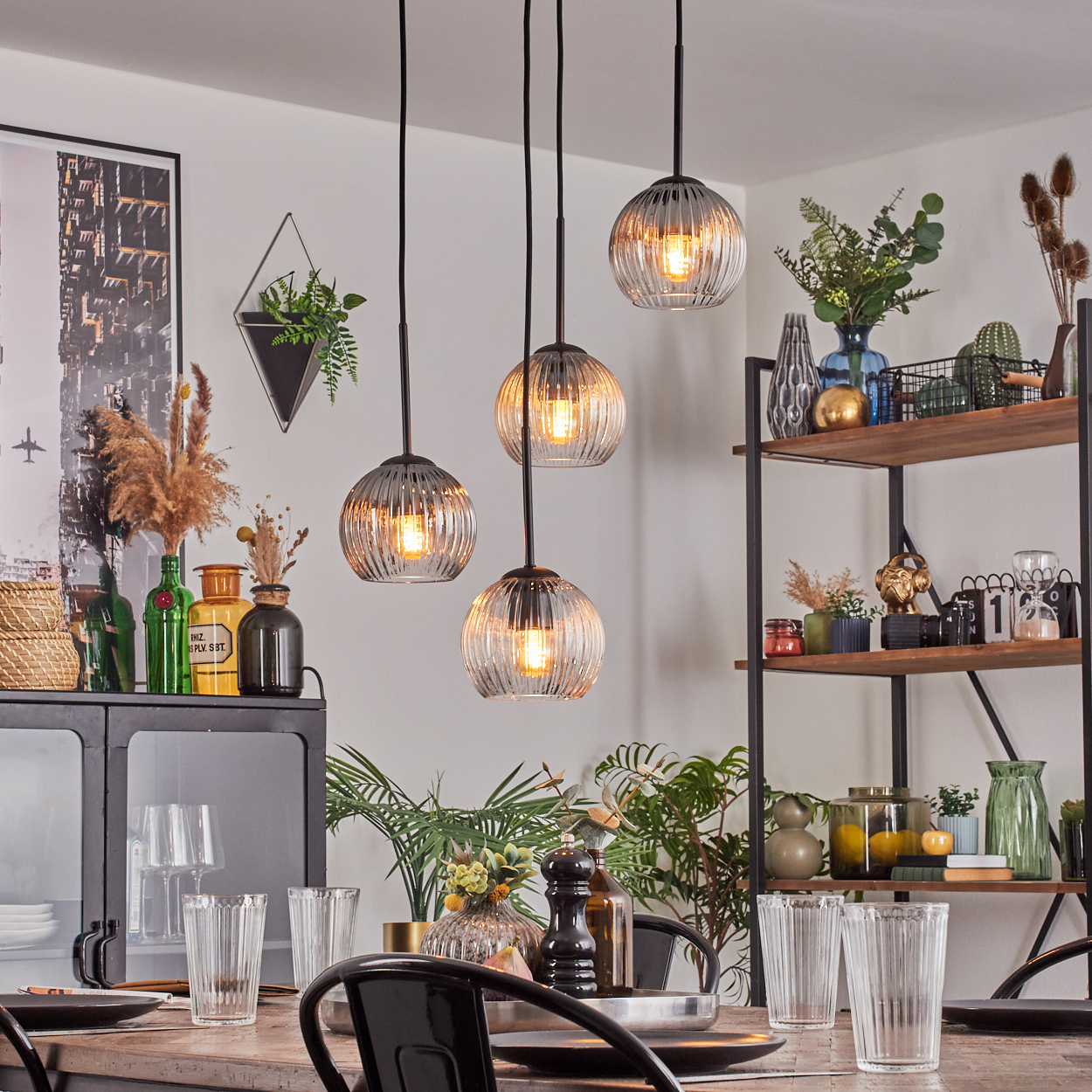 Esszimmer mit Hängelampen, gedecktem Tisch, Regalen mit Dekoration und Pflanzen. Helles, modernes Interieur mit verschiedenen Objekten.