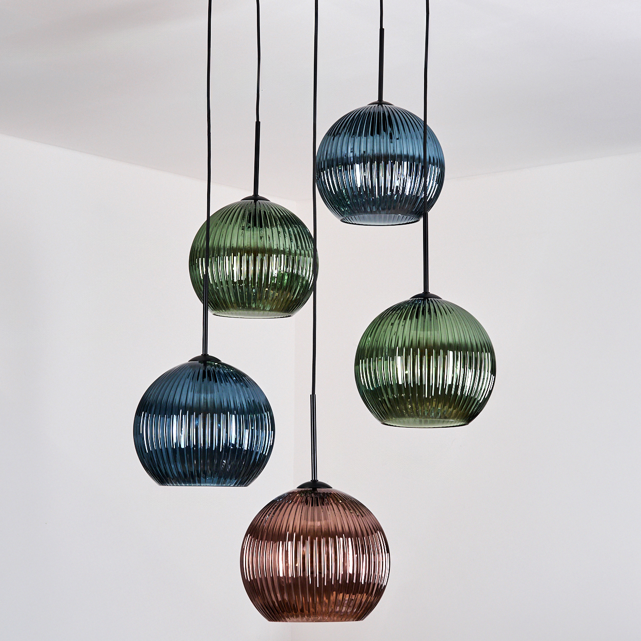 Fünf Glas-Kugel-Pendelleuchten hängen von der Decke. Die Kugeln sind in verschiedenen Farben: Grün, Blau und Kupfer. Der Hintergrund ist weiß.