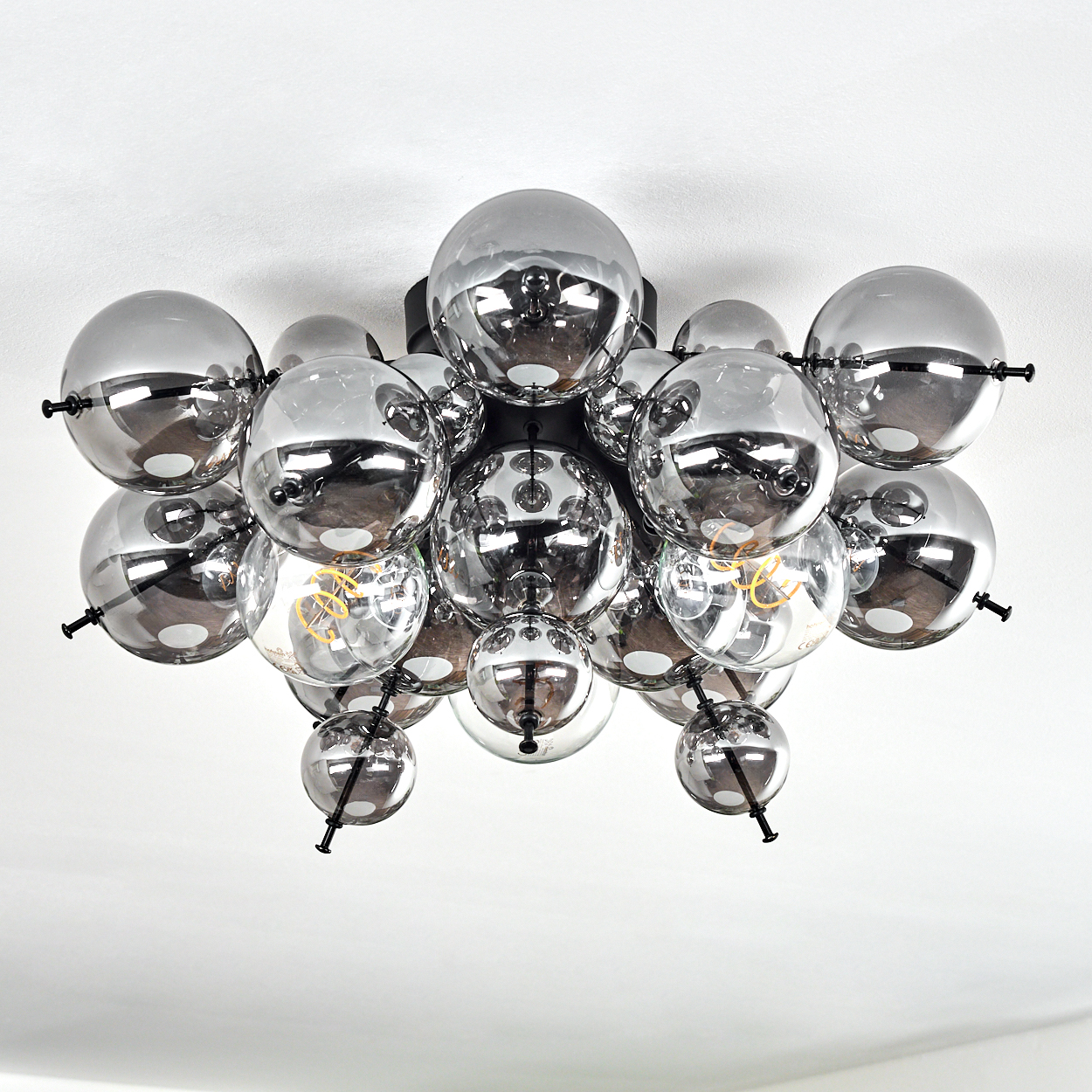 Eine moderne Deckenleuchte mit mehreren rauchigen Glaskugeln und schwarzen Metallarmen vor einer weißen Decke.