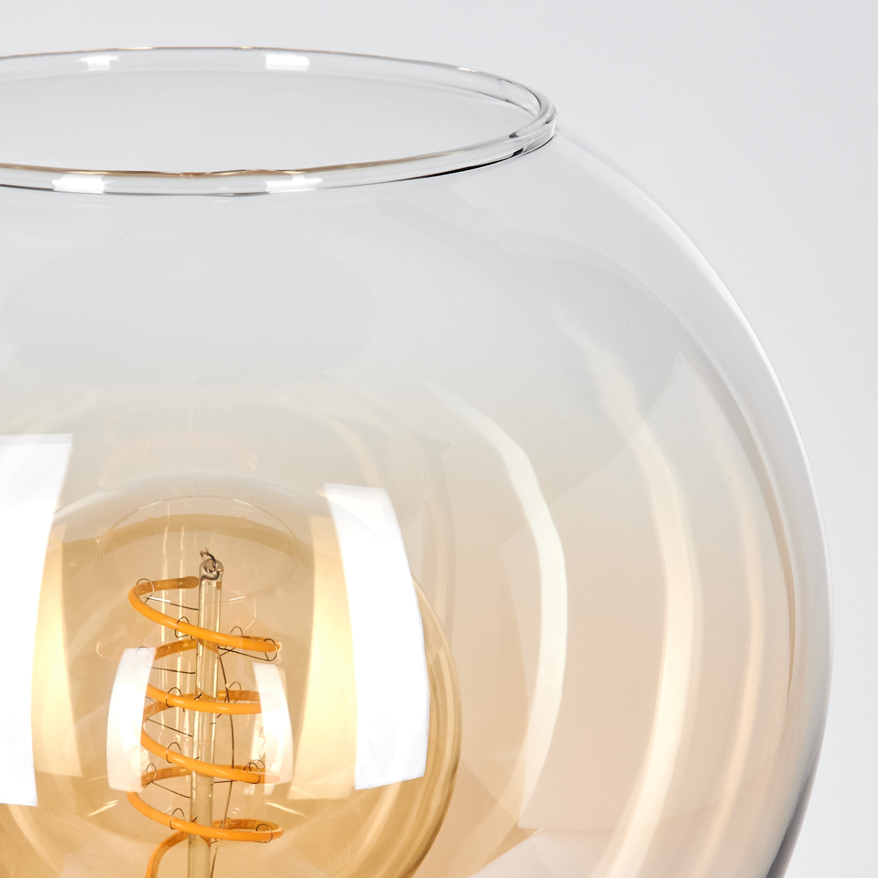 Nahaufnahme einer Glaslampe. Die Lampe hat einen runden, klaren Glasschirm. Im Inneren ist eine warme, orangefarbene Glühbirne sichtbar.