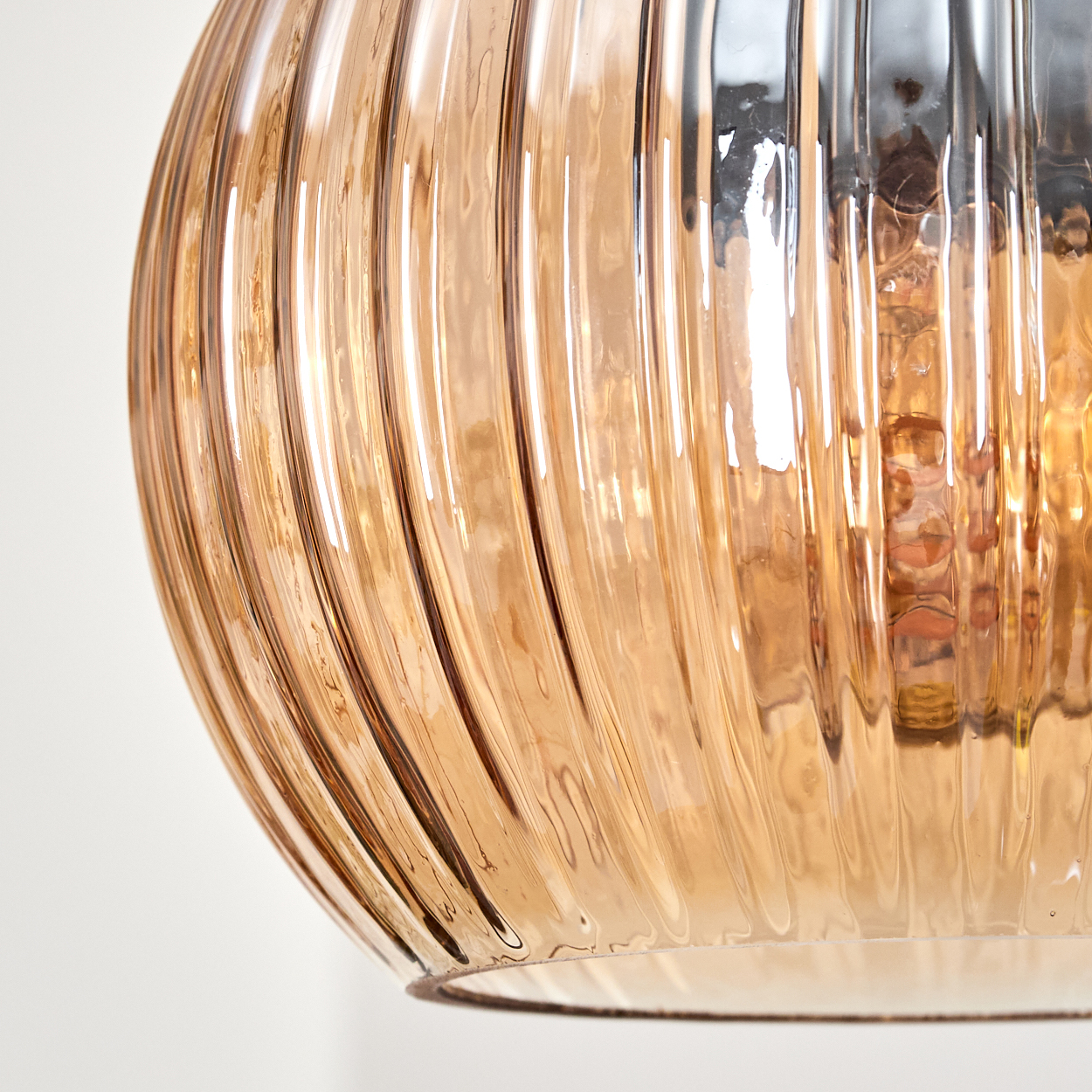 Nahaufnahme einer Glasleuchte. Das bernsteinfarbene Glas hat vertikale Rippen. Der Hintergrund ist weiß.